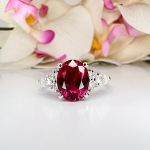 May include: A silver ring with a large oval ruby gemstone surrounded by smaller diamonds.