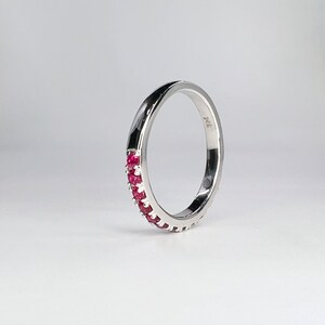 May include: A silver band ring with a row of small red gemstones around the center. The ring is marked "14K" on the inside.