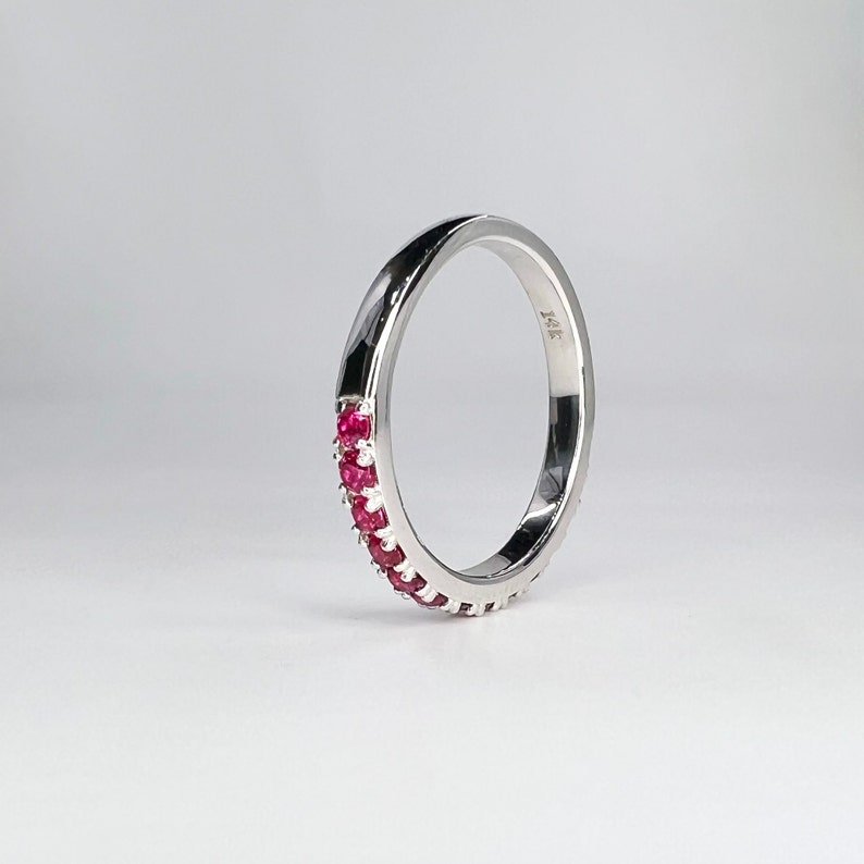 May include: A silver band ring with a row of small red gemstones around the center. The ring is marked "14K" on the inside.