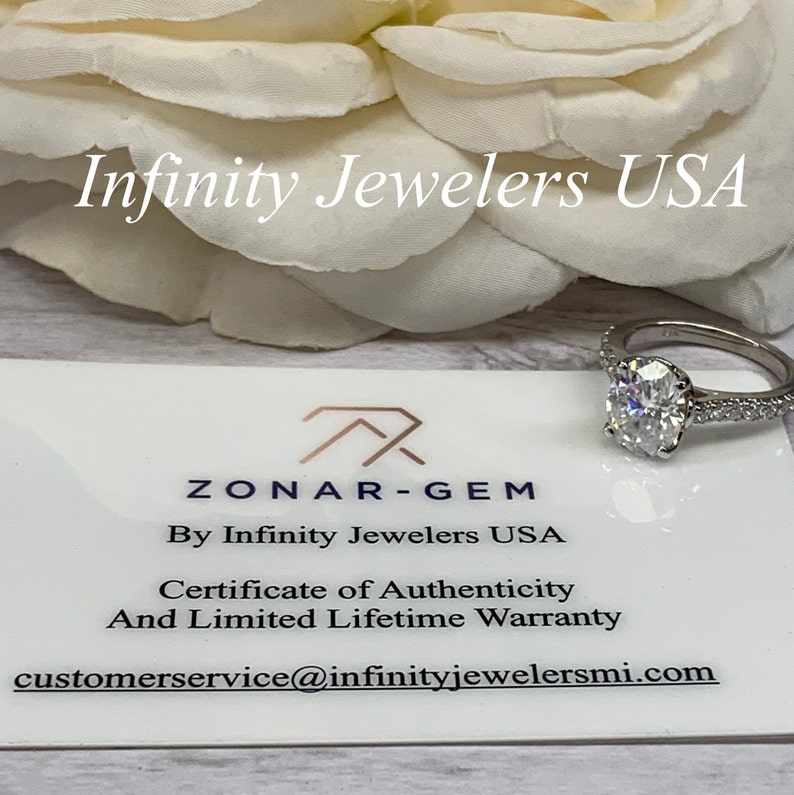 K&ouml;nnte beinhalten: Eine wei&szlig;e Karte mit dem Text "ZONAR-GEM By Infinity Jewelers USA Certificate of Authenticity And Limited Lifetime Warranty customerservice@infinityjewelersmi.com" und ein silberner Ring mit einem gro&szlig;en ovalen Diamanten.