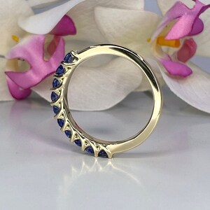 May include: A gold band ring with a row of blue sapphire stones set in a prong setting.