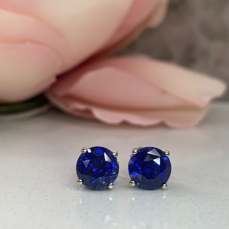 Puede incluir: Un par de pendientes de bot&oacute;n de plata con piedras redondas de color azul oscuro.