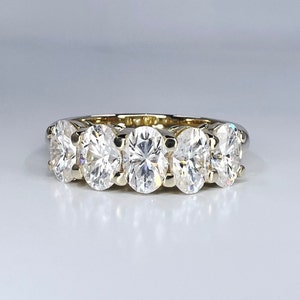 May include: A gold band ring with five oval-shaped diamonds set in a row.