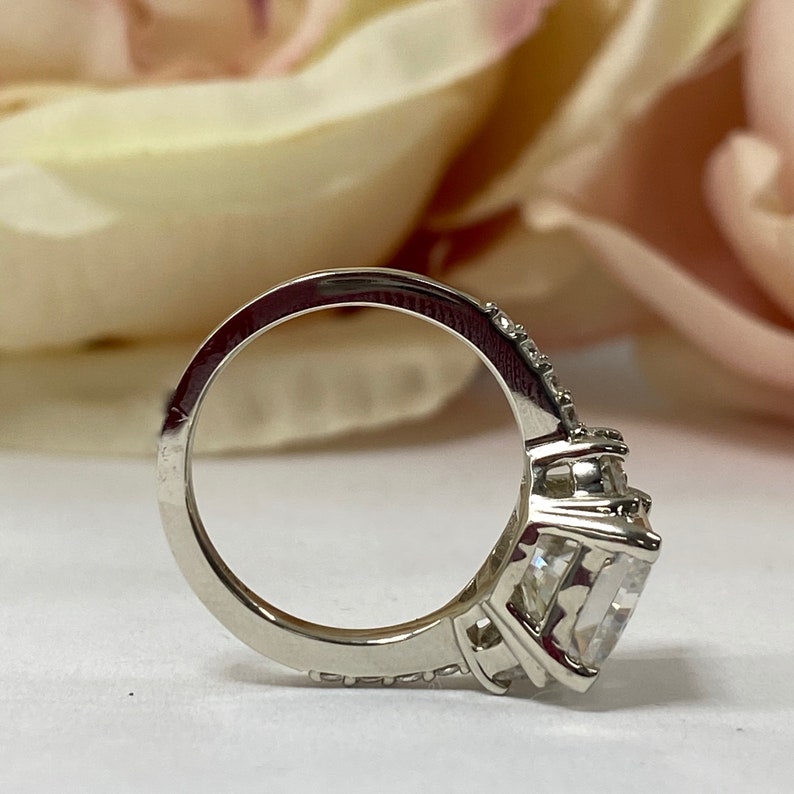 May include: A silver ring with a large, clear, square-shaped gemstone surrounded by smaller gemstones. The ring has a band that is set with smaller gemstones.