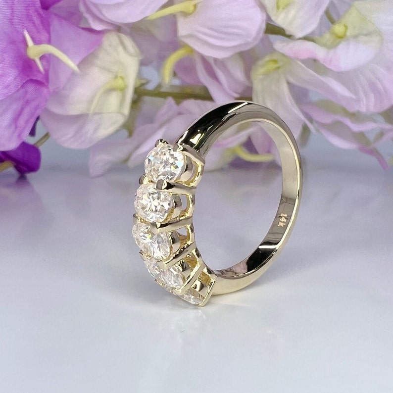 May include: A gold band ring with five round clear stones set in a prong setting. The ring is marked "14K" on the inside.