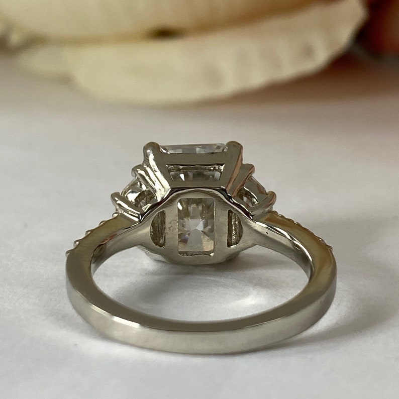 May include: A silver ring with a large, square-shaped, clear gemstone surrounded by smaller, clear gemstones. The ring has a simple band.