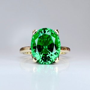 May include: A gold ring with a large, emerald green gemstone. The gemstone is oval-shaped and has a faceted cut.