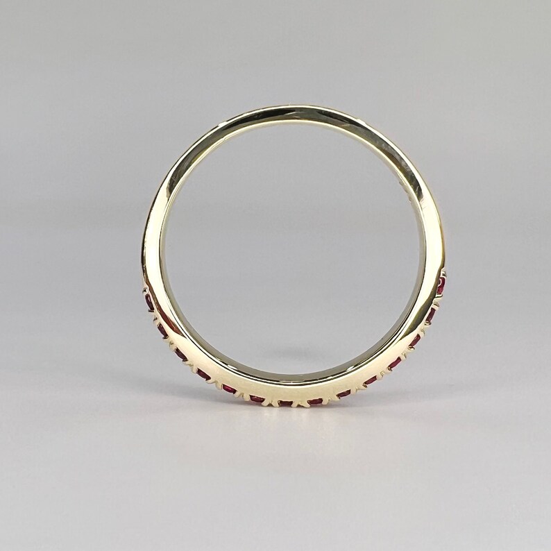 May include: A gold band ring with a row of small red gemstones around the edge.