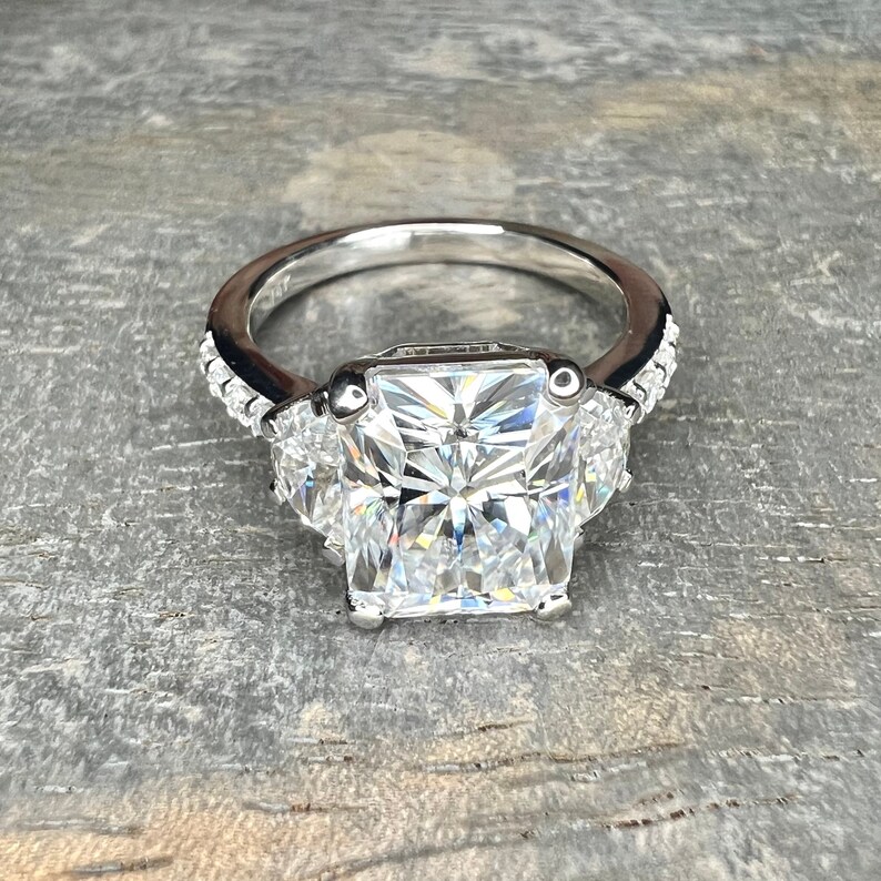 May include: A silver ring with a large square-shaped diamond in the center and two smaller triangular diamonds on either side. The ring is set with smaller diamonds around the band.