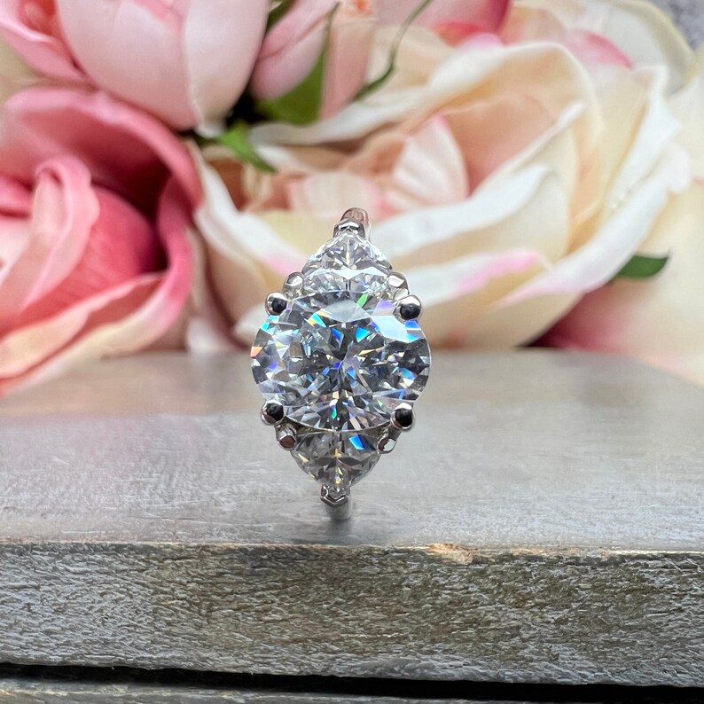 May include: A silver ring with a large, round, clear diamond in the center. Three smaller, pear-shaped diamonds are set on either side of the center stone.