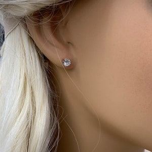 May include: A close-up of a person's ear with a small, round, clear diamond stud earring.