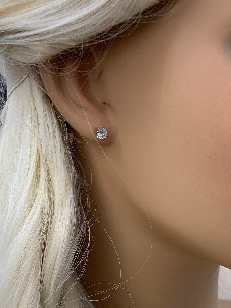 May include: A close-up of a person's ear with a small, round, clear diamond stud earring.