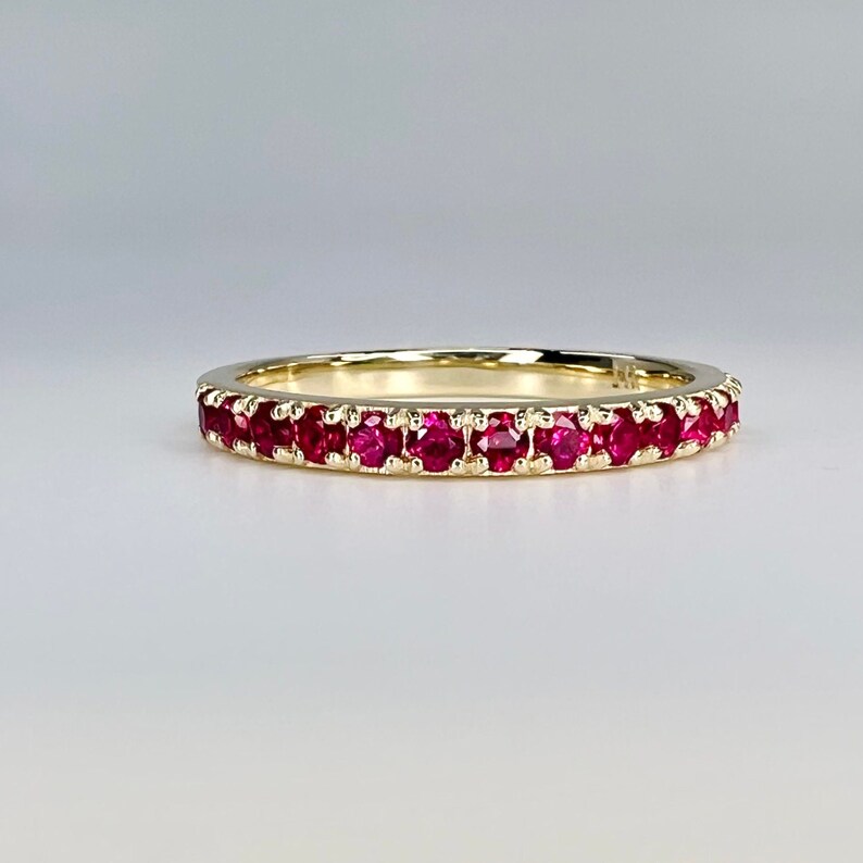 May include: A gold band ring with a row of red ruby stones.