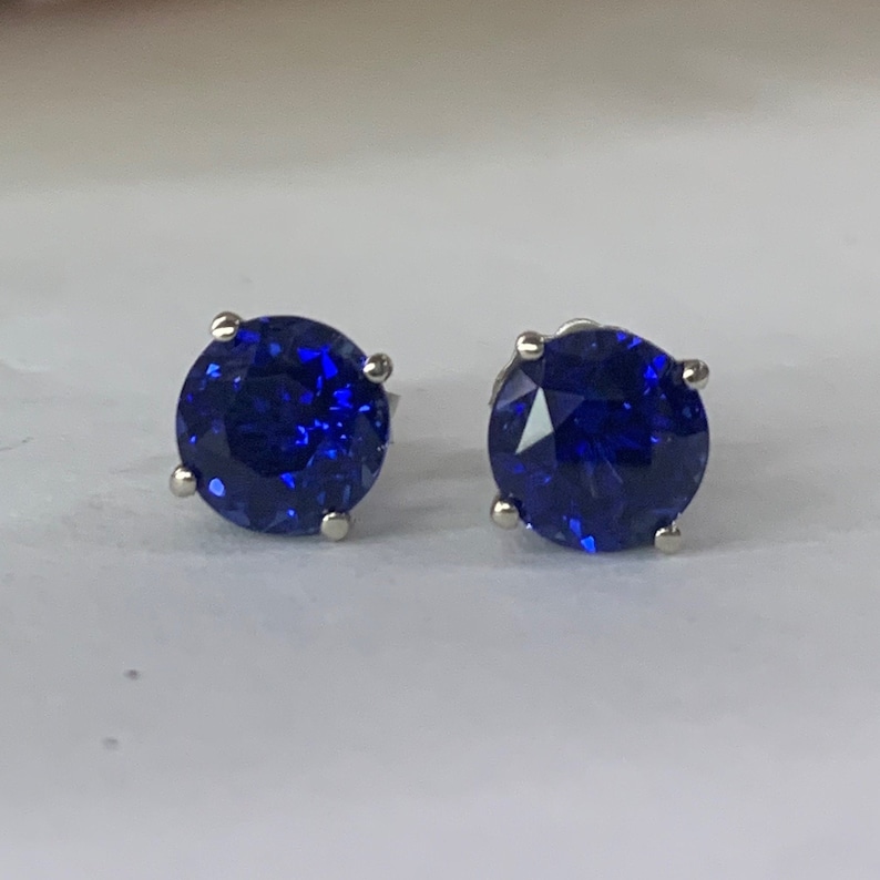 Puede incluir: Un par de pendientes de bot&oacute;n de plata con piedras redondas de color azul oscuro.