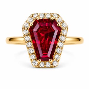 May include: A gold ring featuring a large, faceted, red gemstone in a unique coffin shape, surrounded by a halo of small, sparkling white diamonds. The ring's band is a simple, polished gold.