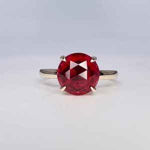 May include: A red gemstone ring with a gold band. The gemstone is a round, faceted ruby.