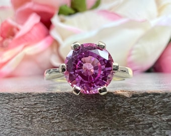 Op de afbeelding: Een zilveren ring met een grote, ronde, paarse edelsteen in een zetting met zes grijpklauwen.