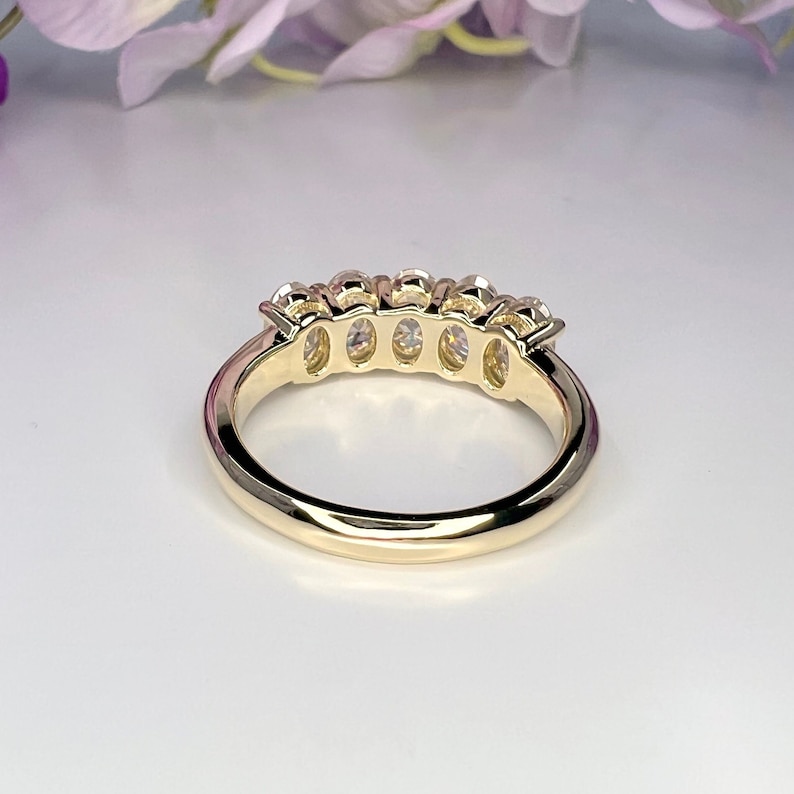 May include: A gold band ring with five oval-shaped gemstones set in a row.