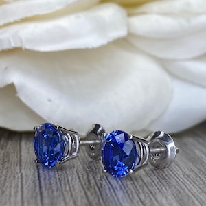 Puede incluir: Un par de pendientes de plata con una piedra preciosa redonda de zafiro azul en cada pendiente.