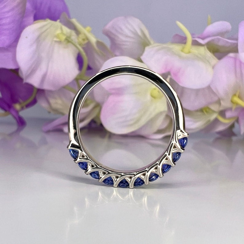 May include: A silver band ring with a row of blue sapphire stones set in a delicate design.