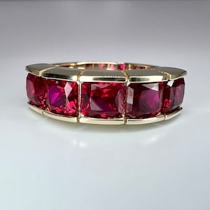May include: A gold band ring with five square-shaped ruby gemstones set in the band.