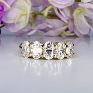 May include: A gold band ring with five oval-shaped clear gemstones.