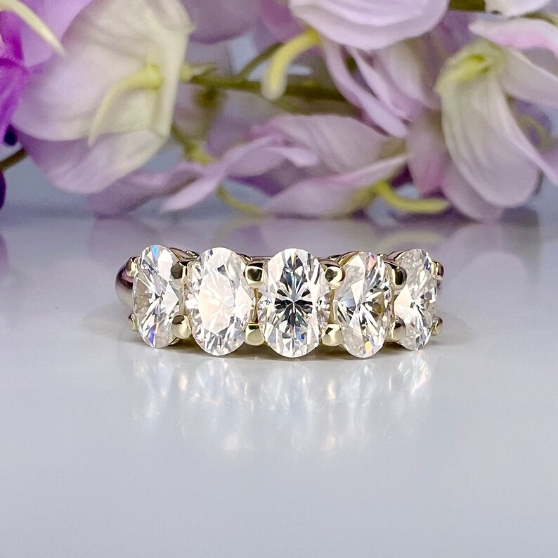 May include: A gold band ring with five oval-shaped clear gemstones.
