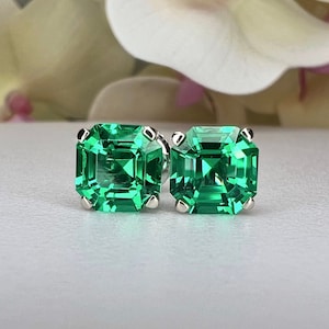May include: A pair of emerald green square-shaped earrings with a silver setting.