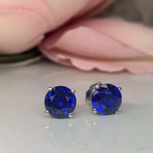 Puede incluir: Un par de pendientes de bot&oacute;n de plata con piedras redondas de zafiro azul.