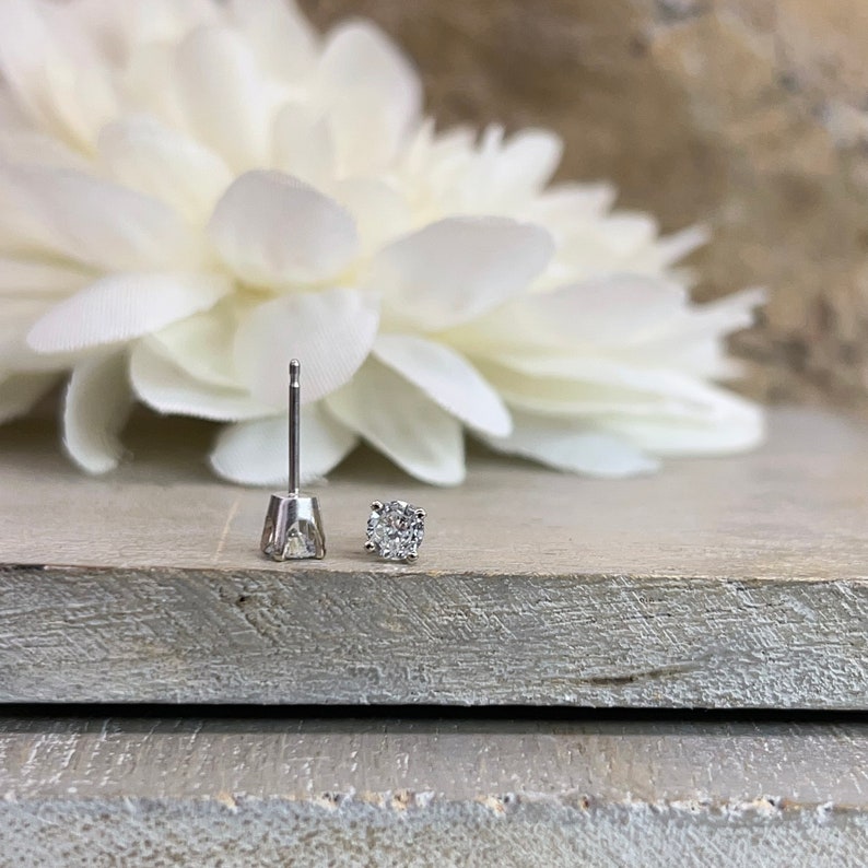 May include: A pair of silver stud earrings with a single round diamond in each earring.