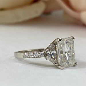 May include: A silver engagement ring with a large, square-shaped, clear center stone and smaller, clear stones set in a band around the center stone.