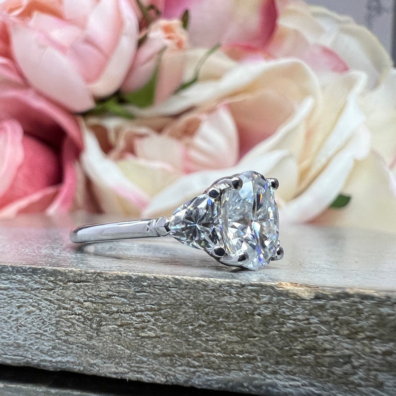 May include: A silver engagement ring with a large oval-shaped diamond and two smaller triangular diamonds on the side.