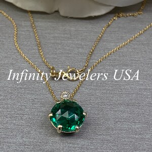 May include: A gold chain necklace with a green gemstone pendant. The pendant is a round, faceted stone with a smaller diamond accent. The text "Infinity Jewelers USA" is visible in the image.