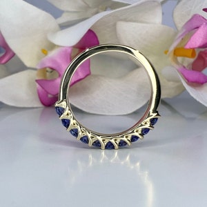 May include: A gold band ring with a row of blue sapphires set in a prong setting.