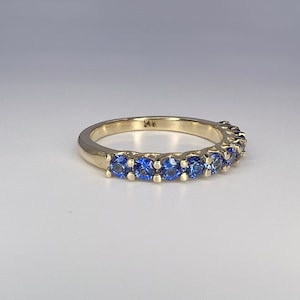 May include: A gold band ring with a row of blue sapphires. The ring is marked "14K" on the inside.