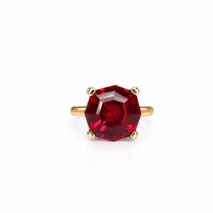 May include: A gold ring featuring a large, faceted, hexagonal-cut deep red gemstone set in a four-prong mounting. The band is smooth and polished, providing a simple foundation for the prominent, geometric, vibrant red center stone.