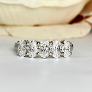 May include: A silver band with five oval-shaped clear gemstones set in a row.