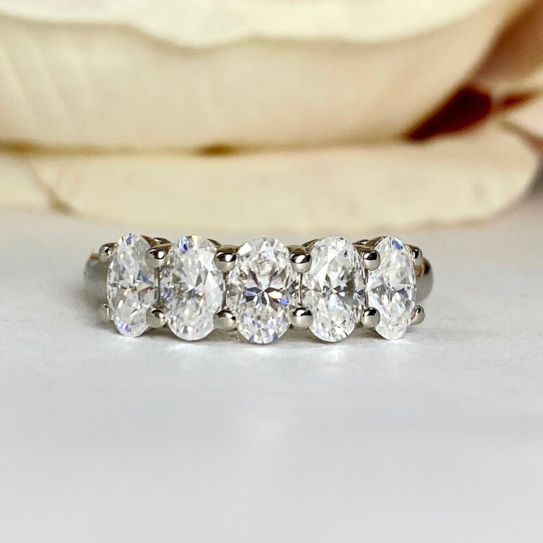 May include: A silver band with five oval-shaped clear gemstones set in a row.