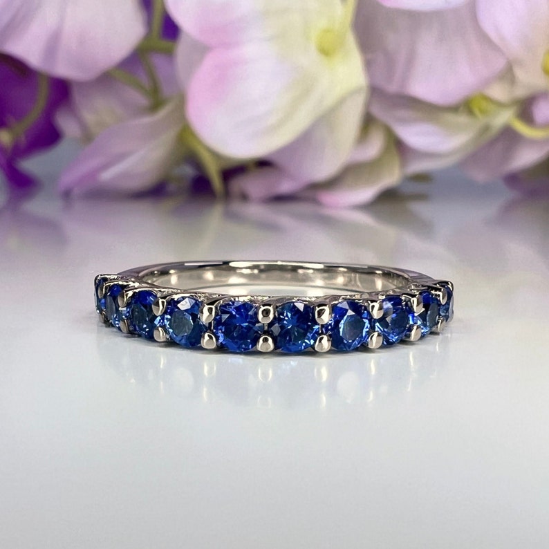 May include: A silver band with a row of blue sapphires set in a prong setting.
