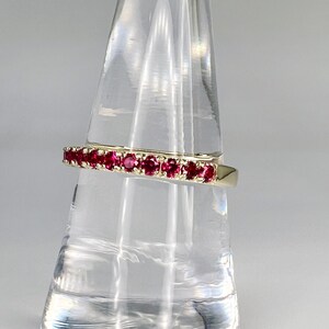 May include: A gold band ring with a row of red ruby stones.