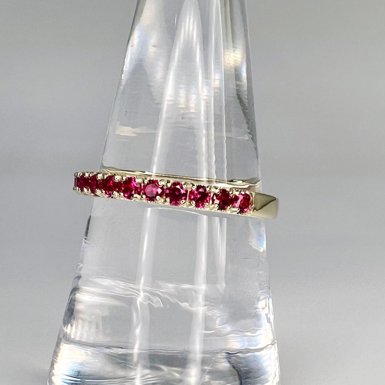 May include: A gold band ring with a row of red ruby stones.