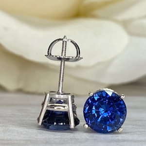 Puede incluir: Un par de pendientes de plata con una piedra preciosa de zafiro redonda de color azul oscuro en cada uno. Los pendientes tienen un dise&ntilde;o simple y cl&aacute;sico.
