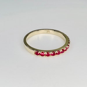 May include: A gold band ring with a row of red ruby stones set in the band. The ring is marked "14K" on the inside.