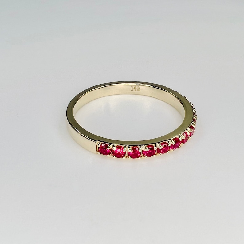 May include: A gold band ring with a row of red ruby stones set in the band. The ring is marked "14K" on the inside.