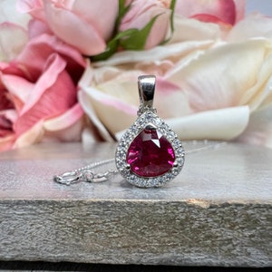May include: A silver pendant necklace with a pear-shaped pink gemstone surrounded by a halo of smaller clear gemstones.