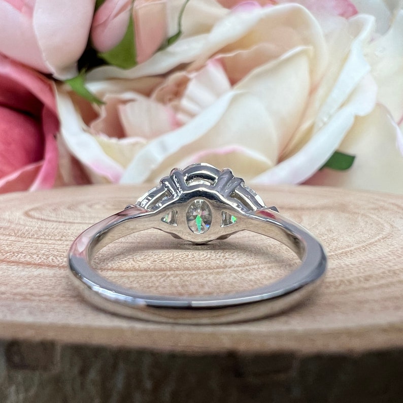 May include: A silver ring with an oval-shaped center stone and smaller stones set in a halo around it. The ring is on a wooden surface.