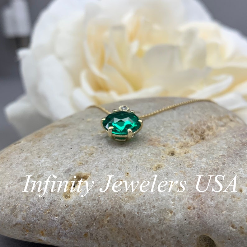 May include: A gold chain necklace with a green gemstone pendant. The pendant is set in a gold prong setting and has a small diamond accent.