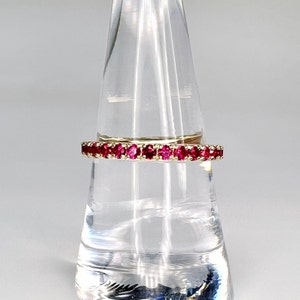 May include: A delicate gold band ring with a row of small, bright red ruby stones.