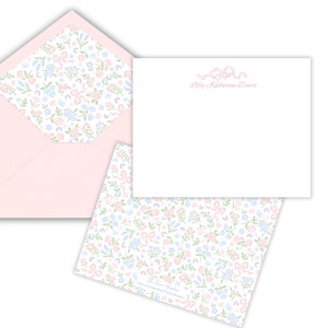 Baby thank you cards - white with dainty pink ribbon at the top and personalization under that in pink script. Back of card has floral bow pattern on the back.  Baby pink envelopes with floral pattern available for liner.