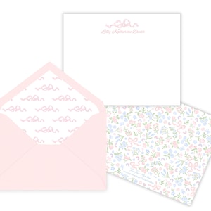 May include: Pink envelope with a white lining featuring a repeating pattern of pink bows. The envelope is open to reveal a white card with the text "Lilly Katherine Davis" in pink script.